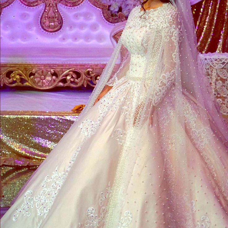 a woman in a white wedding dress standing next to a purple wall with flowers on it