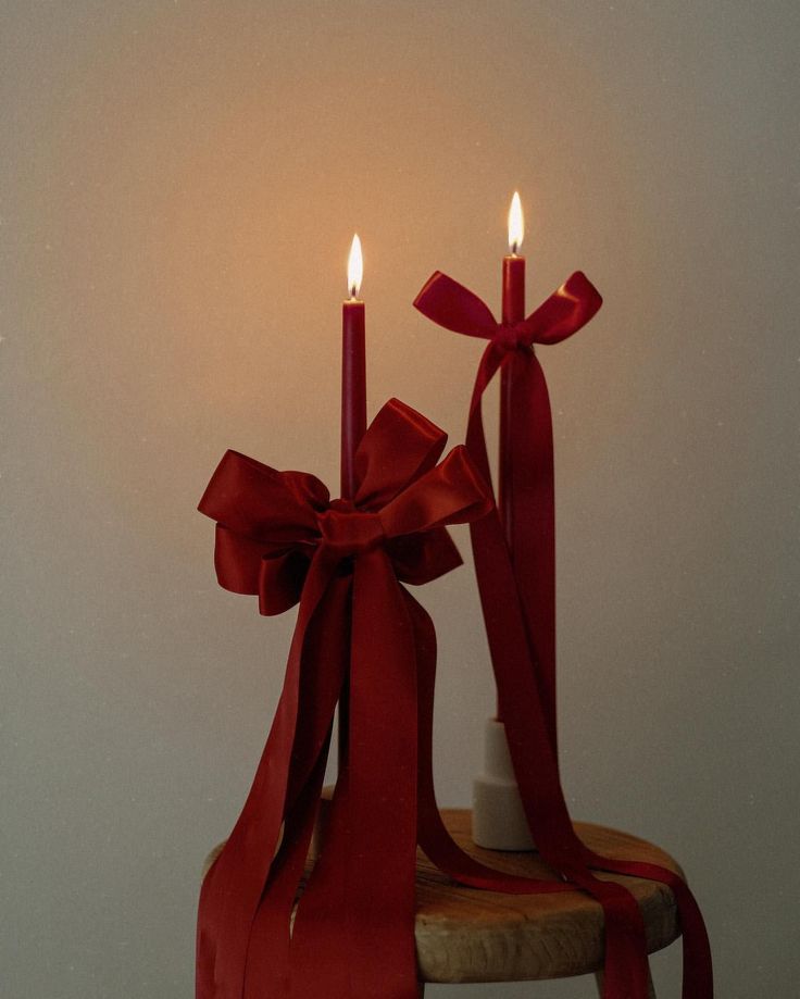 two candles with red ribbons on a table