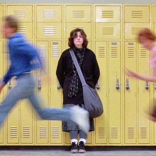 a woman standing in front of lockers with her leg up on the floor and another person walking by