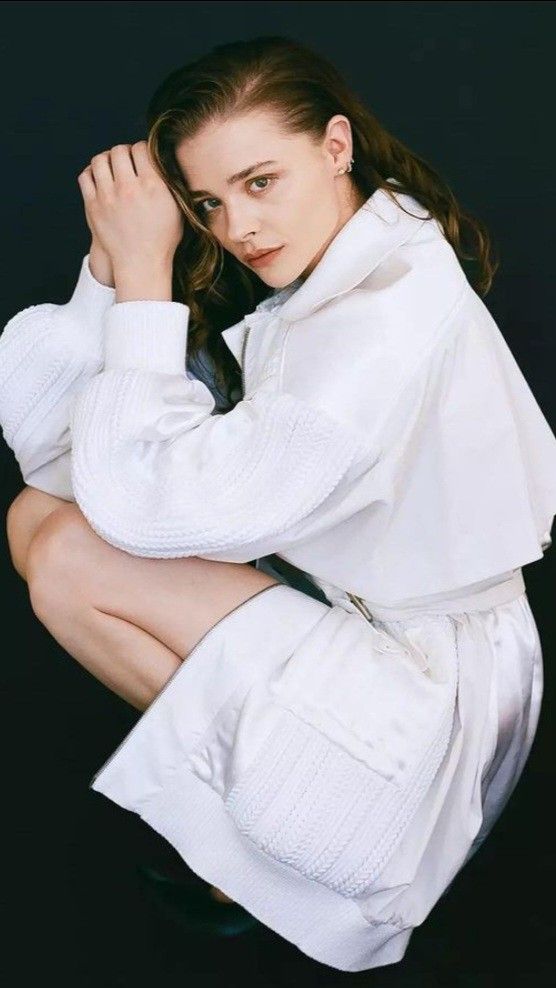 a woman is sitting on the ground wearing white clothing and posing with her hands behind her head