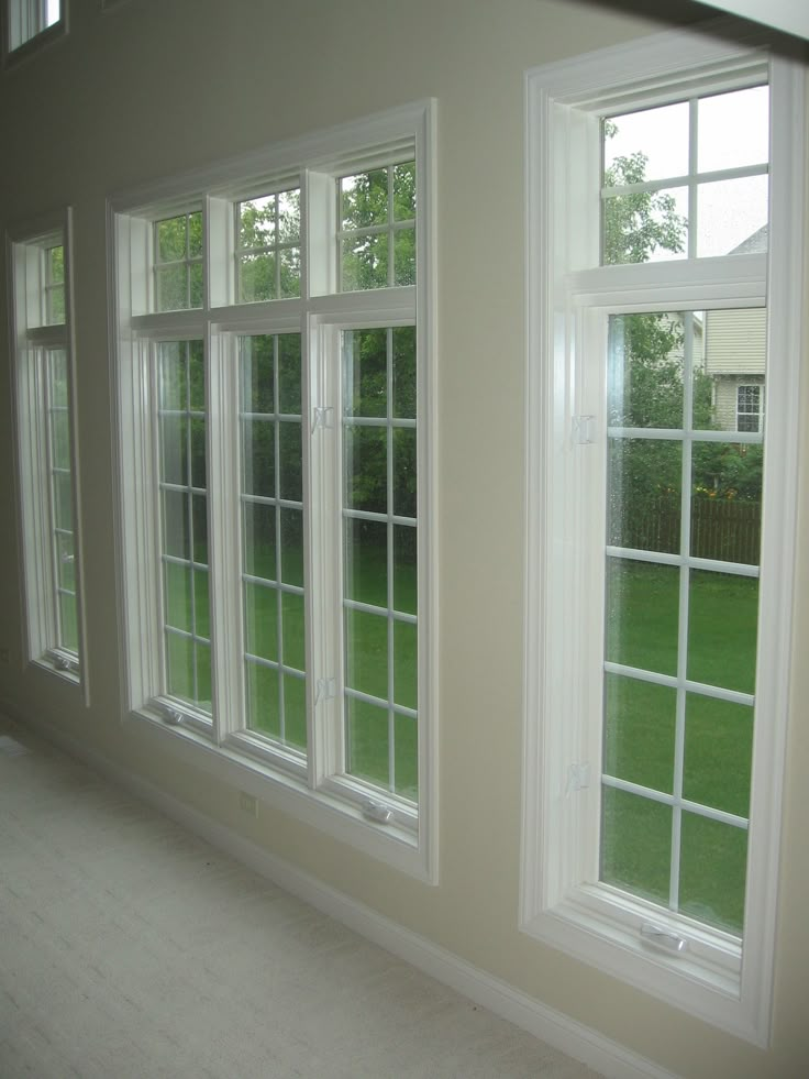 three windows are shown in the corner of a room with white walls and carpeted flooring