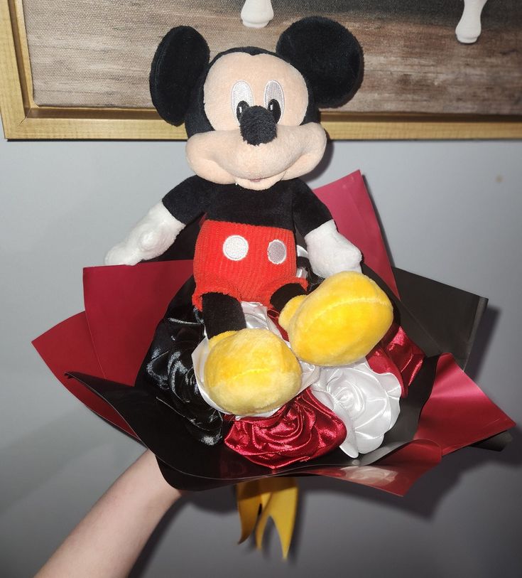 a stuffed mickey mouse holding a bouquet of flowers in front of a painting on the wall