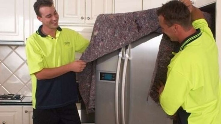 two men in yellow shirts and black pants are looking into a silver refrigerator freezer