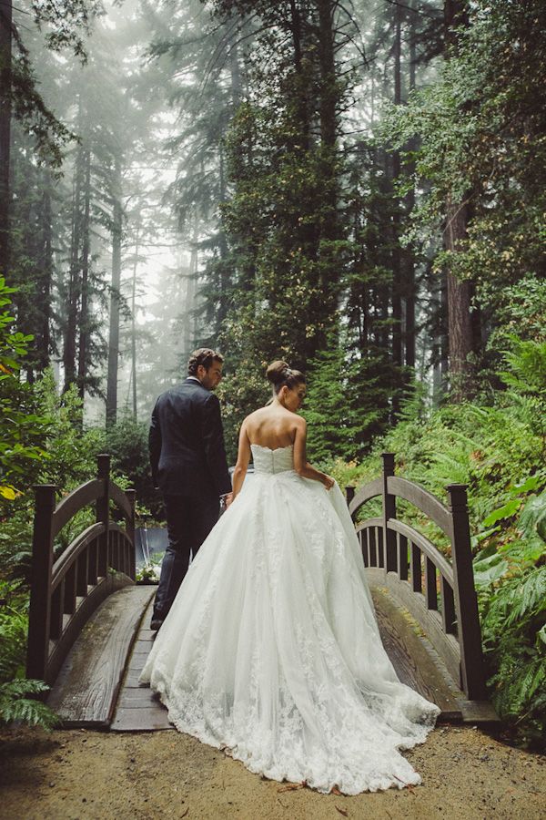 a bride and groom standing on a bridge in the woods