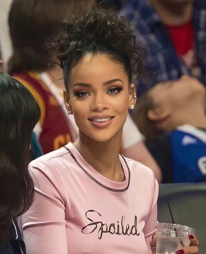 a woman in pink shirt sitting next to another person at a basketball game and holding a drink