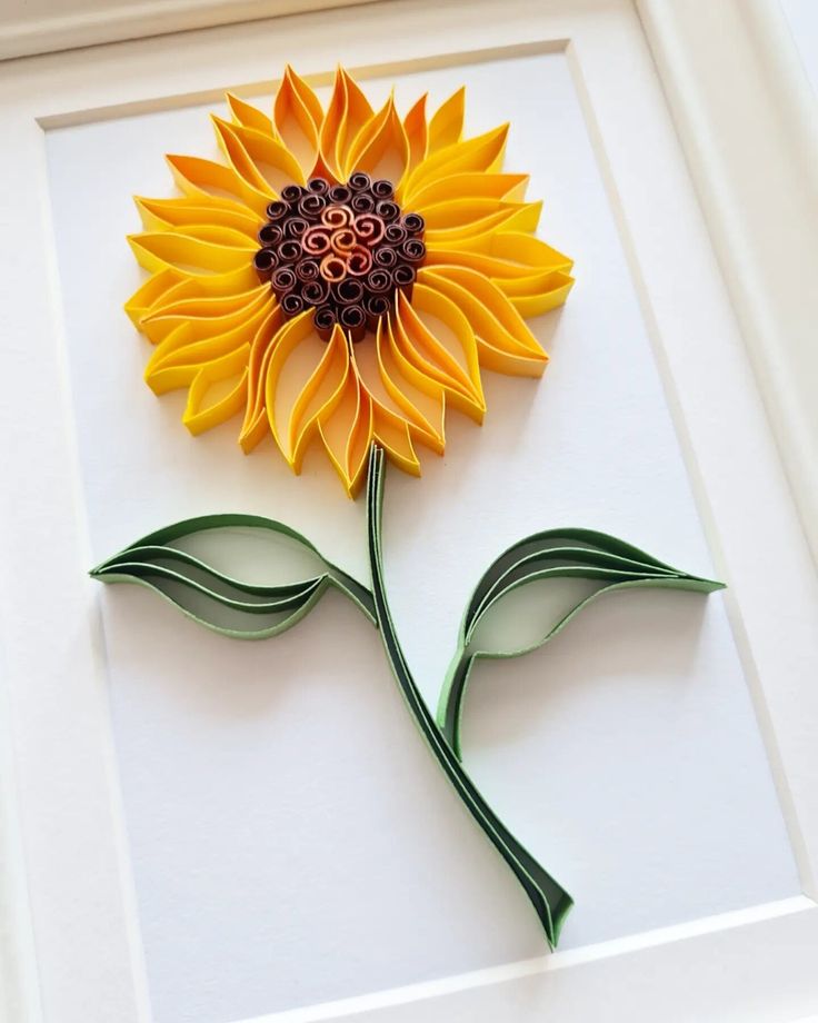 a sunflower made out of paper sitting on top of a white frame