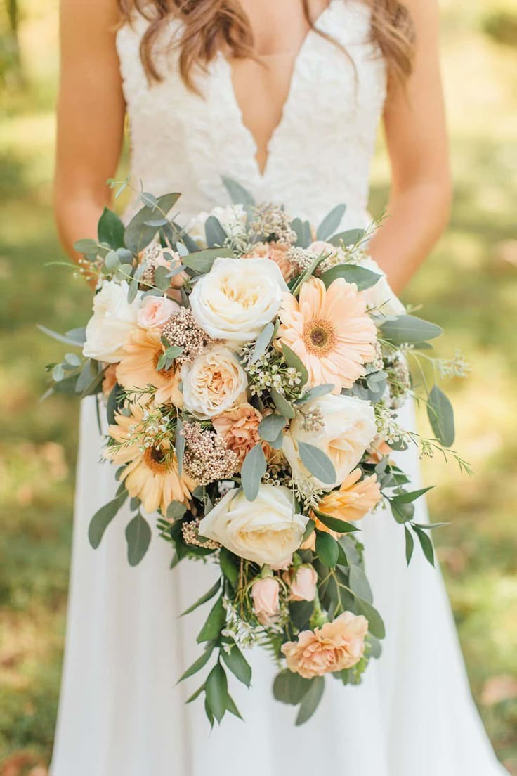 a bridal holding a bouquet of peach and white flowers with greenery on it