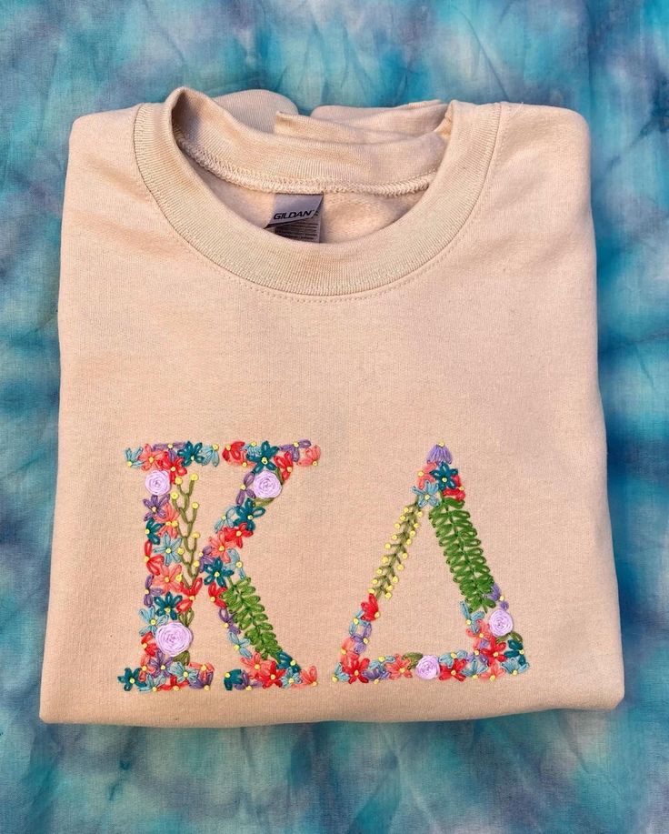 a t - shirt with the letters k and a flowered design on it sitting on a blue background