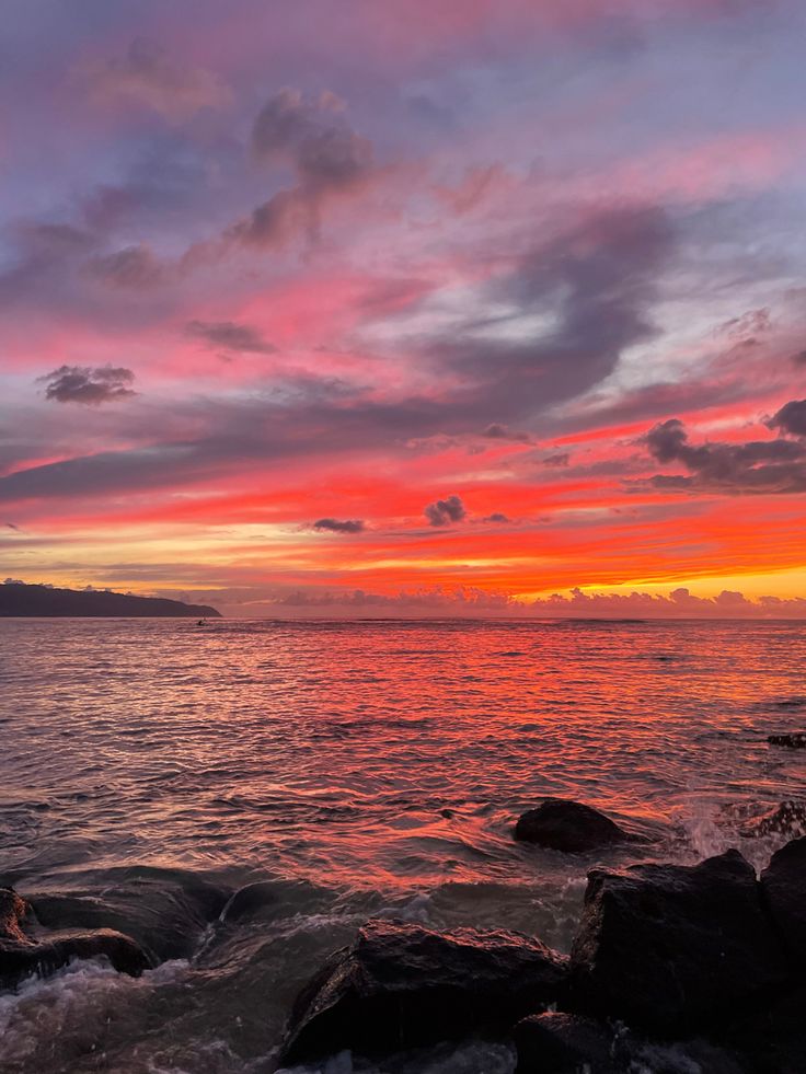 the sun is setting over the water and rocks