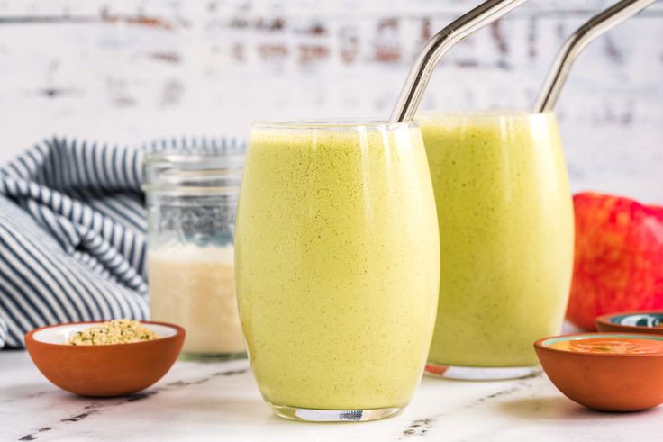 two glasses filled with green smoothie sitting on top of a counter