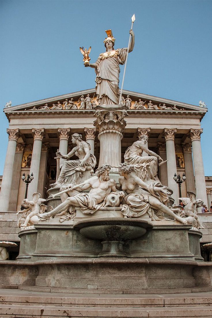 the statue is in front of an old building with columns and statues on it's sides