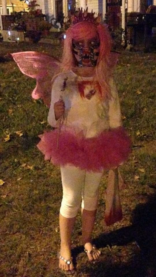 a woman with pink hair and makeup is dressed up as a fairy in front of a house