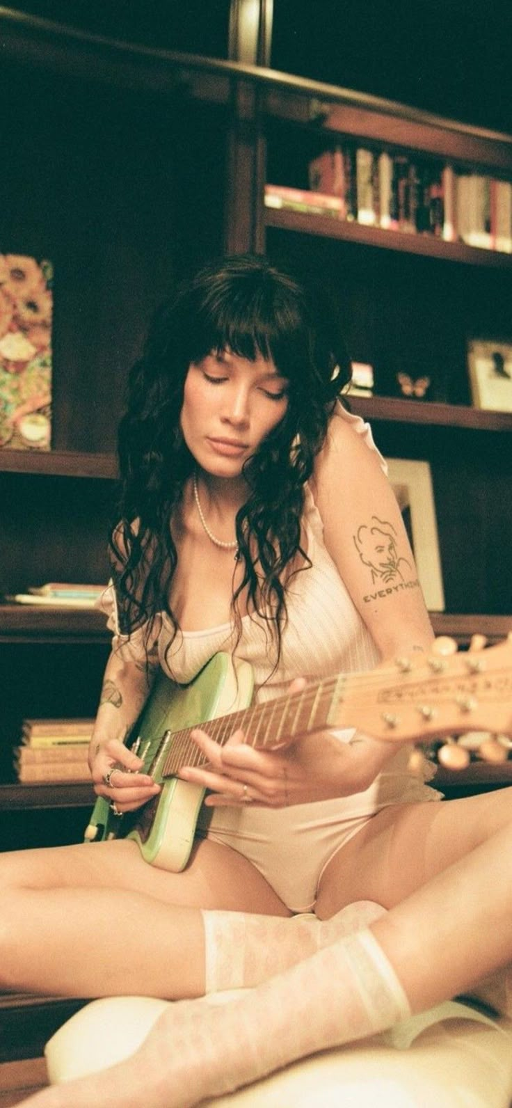 a woman sitting on the floor with a guitar in her hand and stockings around her ankles