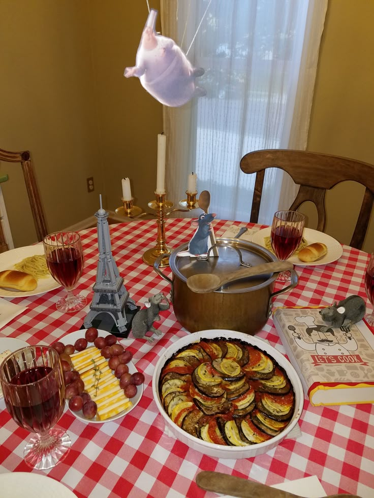 a table topped with plates and bowls filled with food next to a wine glass on top of a red checkered table cloth