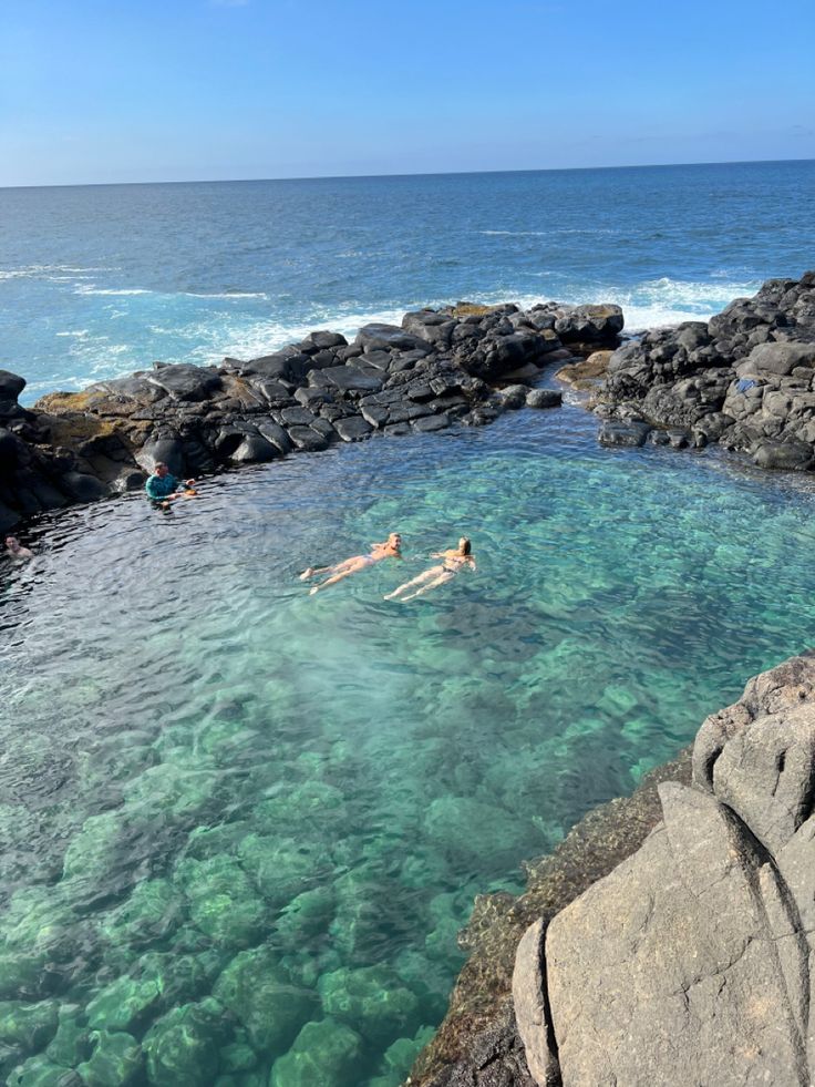 two people swimming in the ocean near rocks