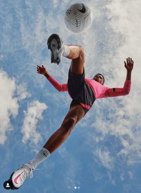 a man in pink shirt and black shorts playing with soccer ball under cloudy blue sky