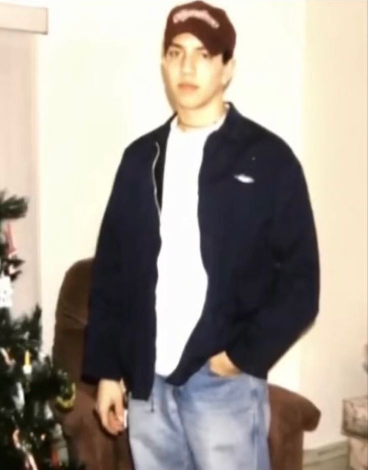 a man standing in front of a christmas tree with his hands in his pockets and looking at the camera