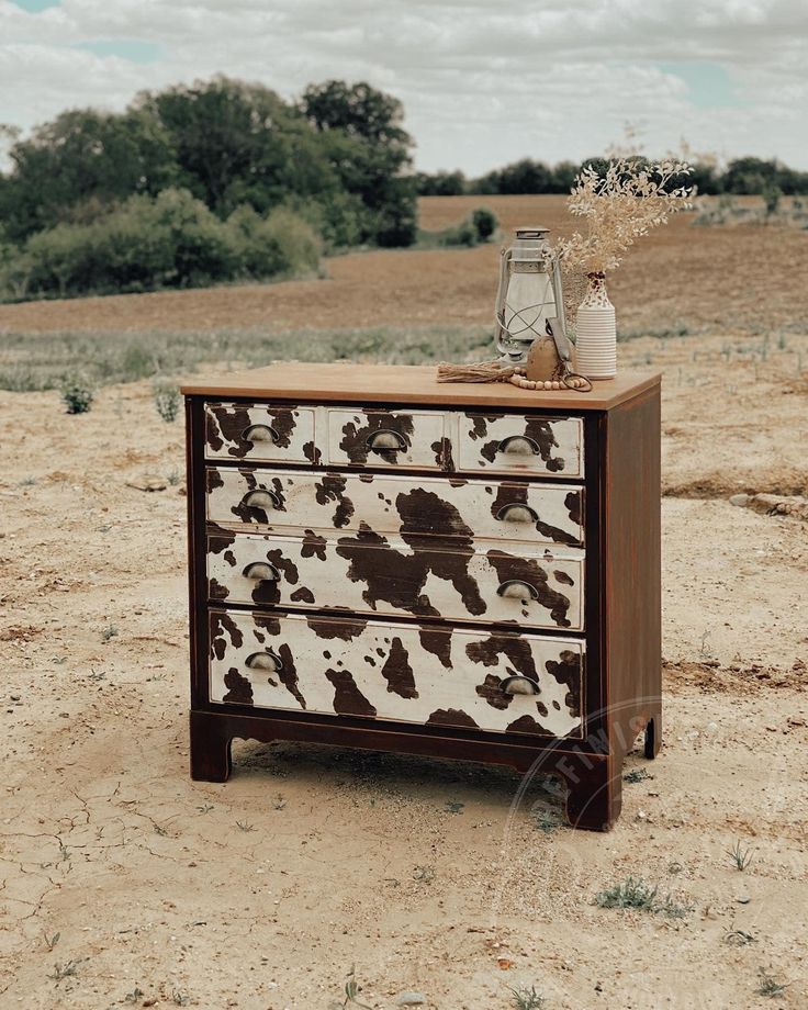 a cow print dresser sitting on top of a dirt field