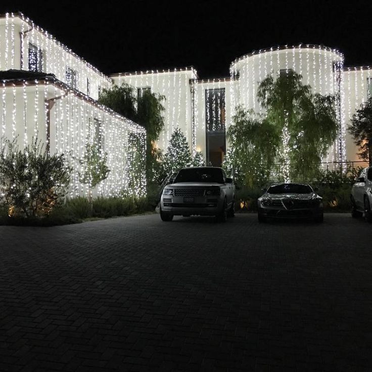 two cars parked in front of a large building with christmas lights on it's sides