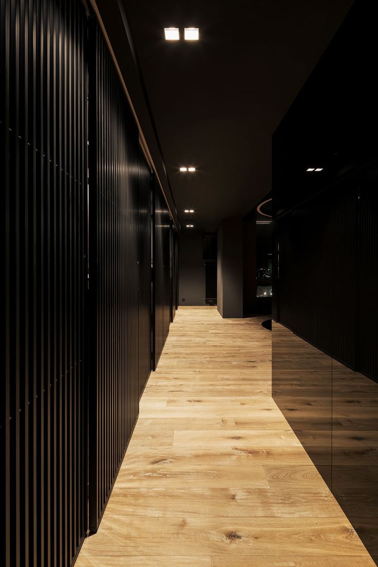 an empty hallway with black walls and wooden flooring is lit by recessed lights