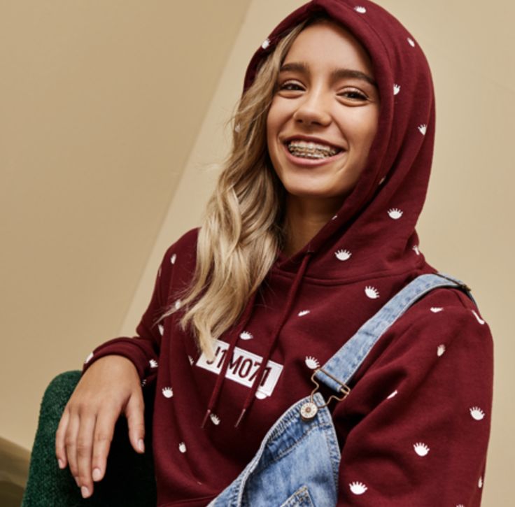 a woman wearing a red hoodie with white hearts on it, sitting in a chair