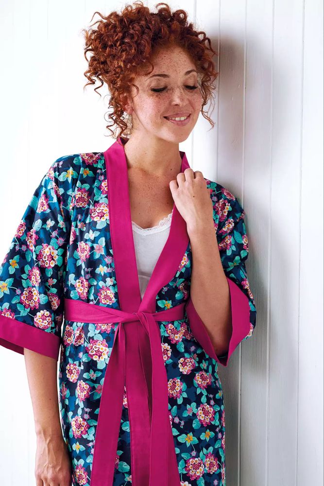 a woman standing next to a white wall wearing a robe with pink ribbon around the waist