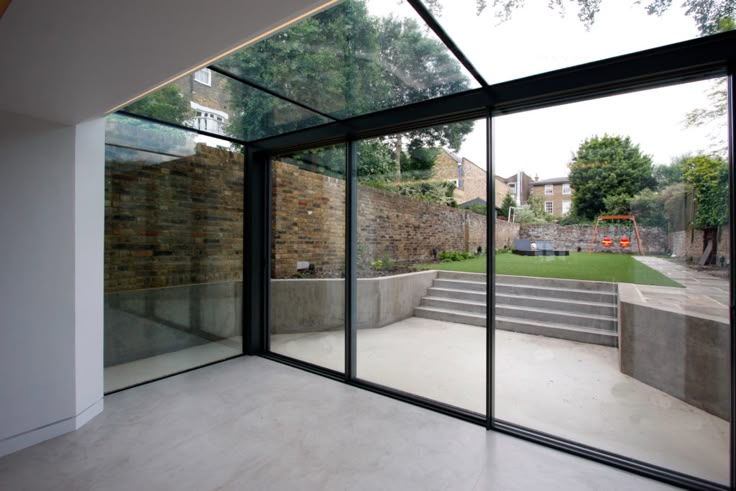 an empty room with glass walls and steps leading up to the back yard, in front of a stone wall