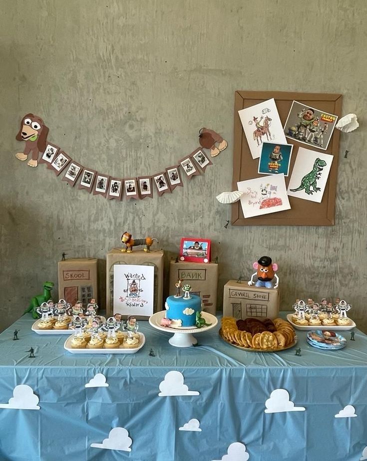 a blue table topped with lots of desserts next to a wall covered in pictures