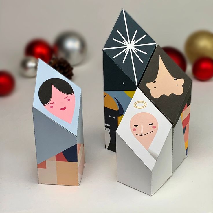 two paper houses with faces on them next to christmas decorations and balls in the background