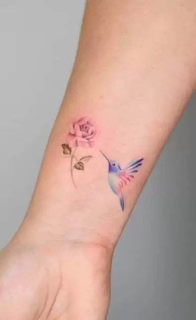 a small tattoo on the wrist of a woman with a pink rose and hummingbird