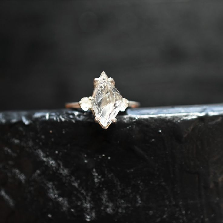 a close up of a ring on top of a black piece of wood with a diamond in the middle