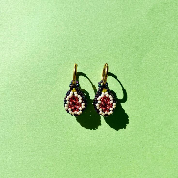 two pairs of earrings sitting on top of a green surface, one with red and white beads