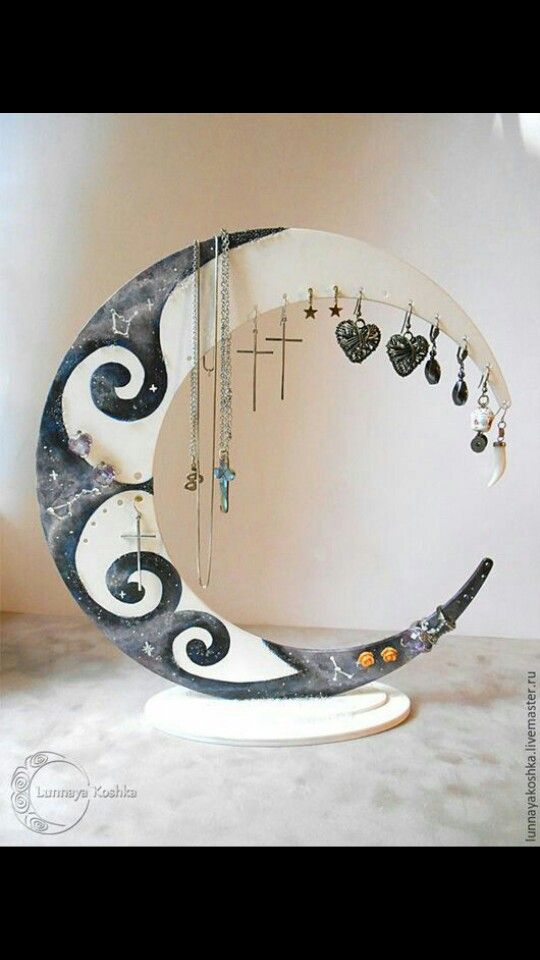 a crescent shaped mirror with jewelry hanging from it's sides and a cross on the other side