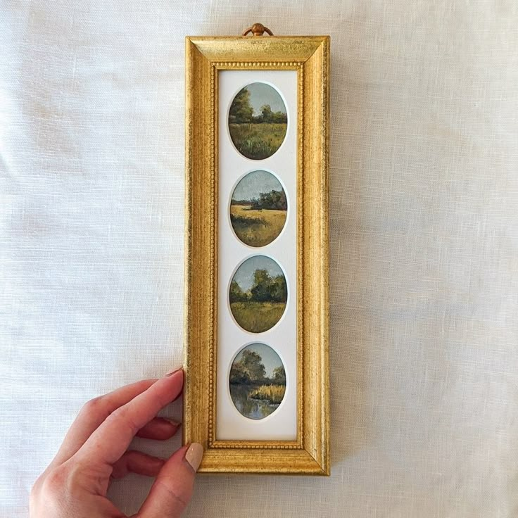 a person holding up a framed painting with four pictures in the frame on top of it