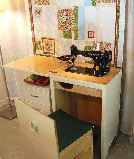 a sewing machine sitting on top of a wooden table next to a white cabinet with drawers