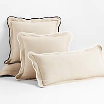 three white pillows with black piping on the bottom and one in beige, sitting next to each other