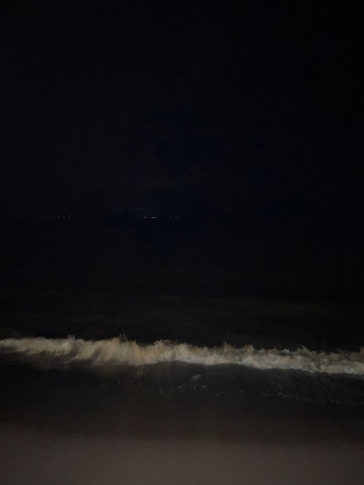 a man riding a surfboard on top of a wave in the ocean at night