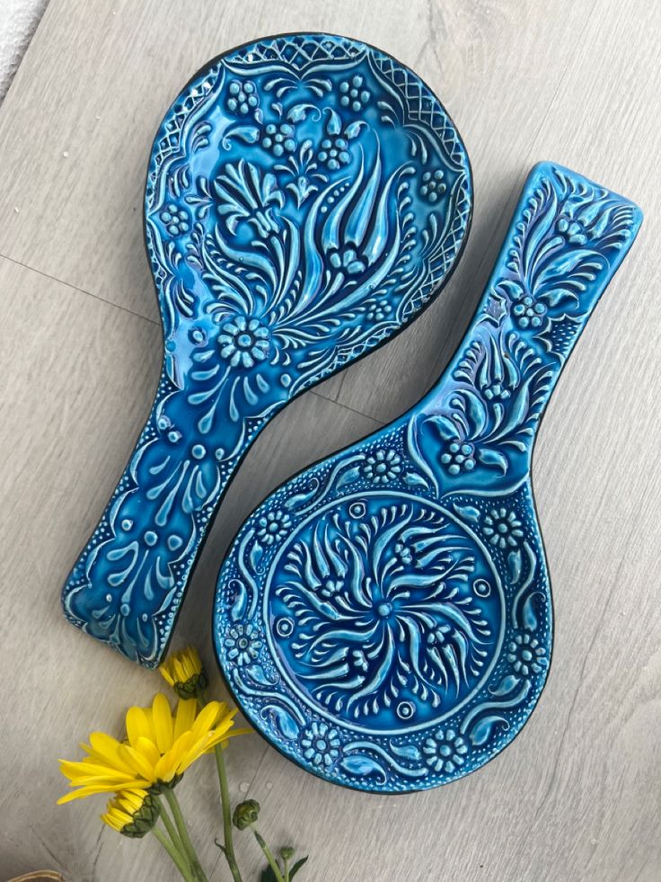 two blue ceramic spoons sitting on top of a table next to a yellow flower