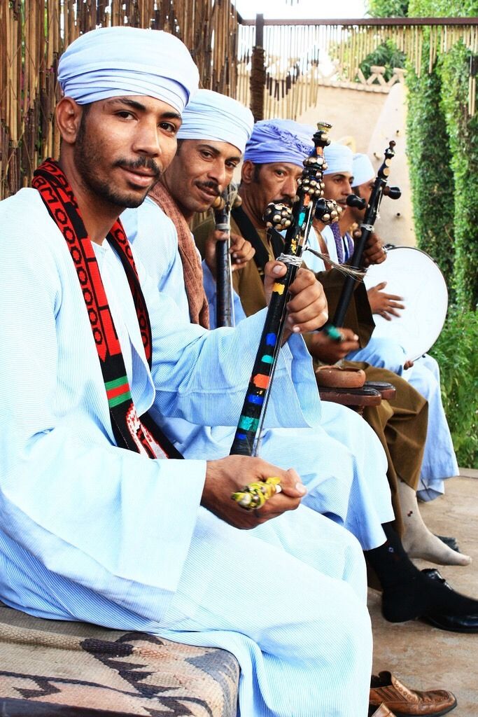 four men sitting on a bench with musical instruments in their hands and wearing turbans