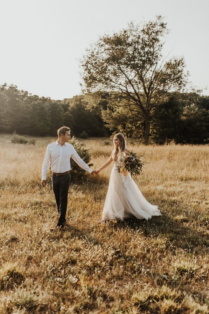 a bride and groom holding hands walking through the grass in an open field at sunset