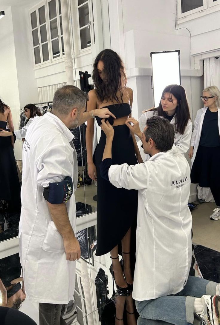 a group of people standing around each other in front of a mirror with one person adjusting the woman's dress