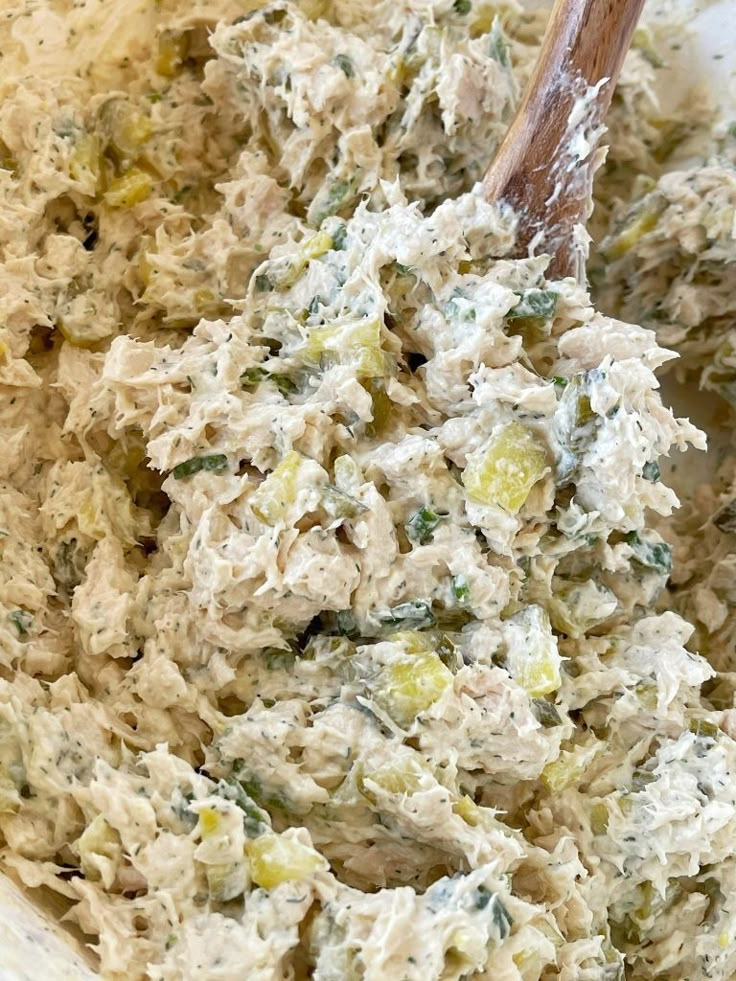 a wooden spoon in a white bowl filled with chicken and spinach salad dressing, ready to be mixed together