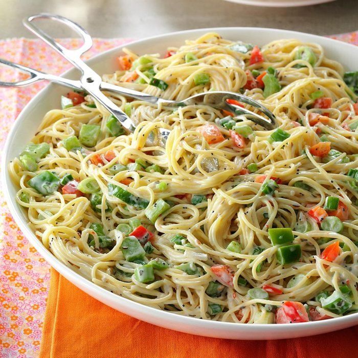 a white bowl filled with pasta and vegetables on top of a orange place mat next to a fork