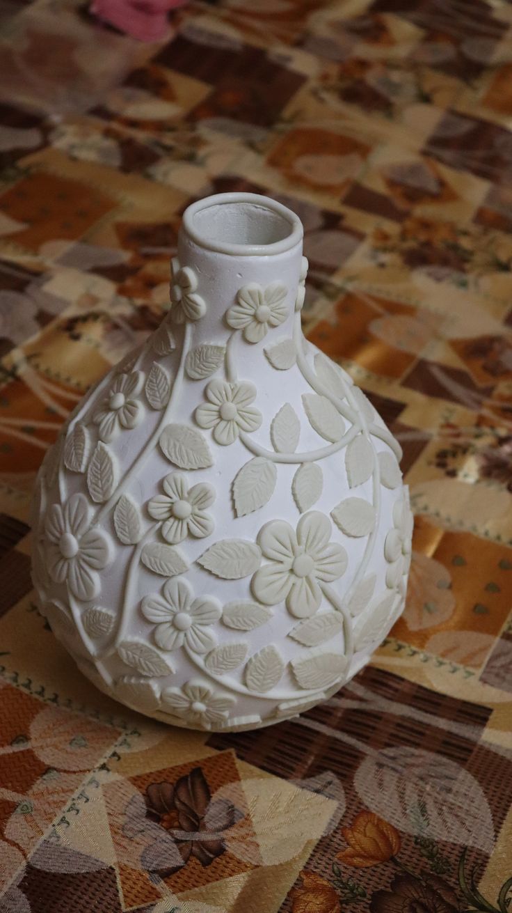 a white vase sitting on top of a quilted tablecloth covered floor next to pink flowers