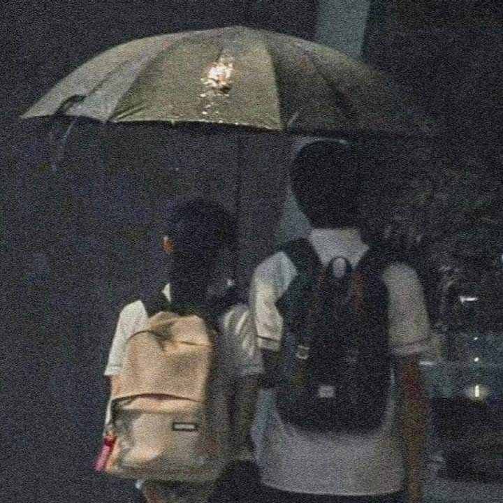 two people walking under an umbrella in the rain on a city street with backpacks