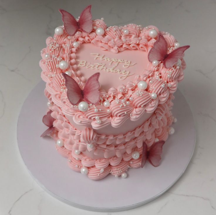 a pink heart shaped cake with butterflies on it's top and the words happy birthday written in white