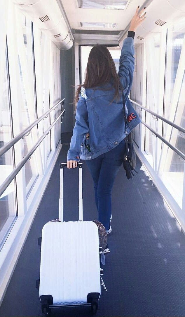 a woman is walking with her luggage down the hall way and waving to someone in the distance