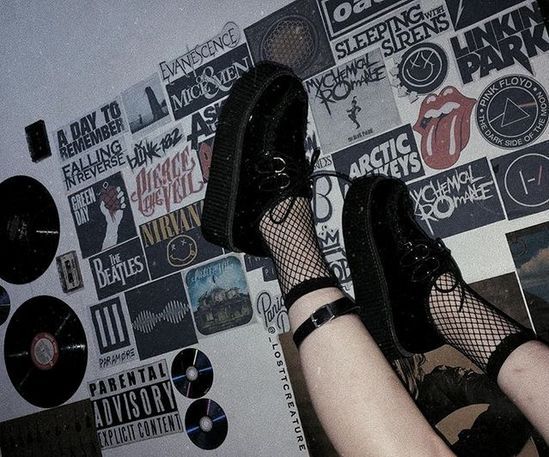 a woman's legs in fishnet stockings and black shoes against a wall covered with records