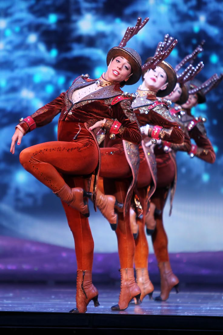 two dancers dressed in red and orange are performing on stage with their arms around each other