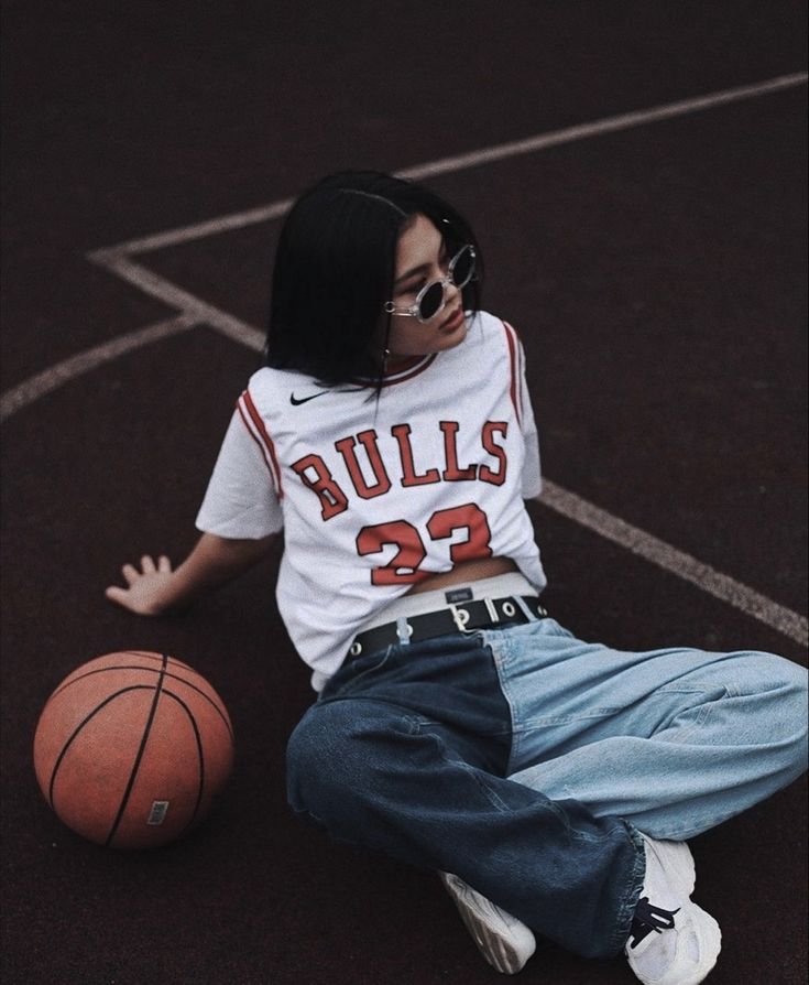 a woman sitting on the ground with a basketball in front of her and wearing sunglasses